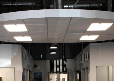 Modern industrial hallway with white walls and ceiling lights. Large letters spell "WHE" above a doorway.