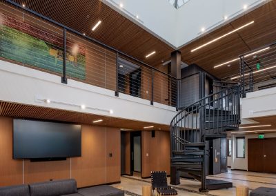 Modern atrium with spiral staircase, large screen, artwork, and wooden ceiling, featuring natural light.