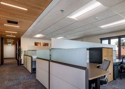 Modern office with cubicles, ergonomic chairs, and indirect lighting. Wood accents on ceiling and walls.