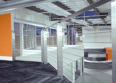 Modern office interior with orange accents, metal railings, exposed ducts, and a curved reception desk.