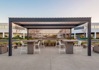Modern outdoor pergola with bar tables and high chairs on a patio.