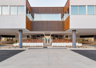 Modern building entrance with a minimalist design, featuring large windows, wood paneling, and landscaped pathways.