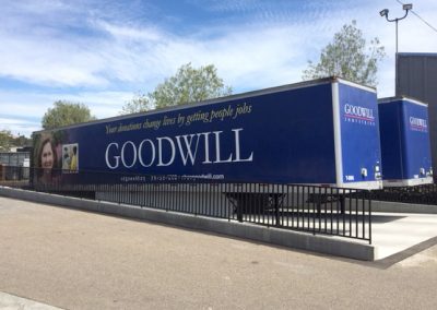 Two Goodwill donation trailers parked in an outdoor lot under a clear sky.