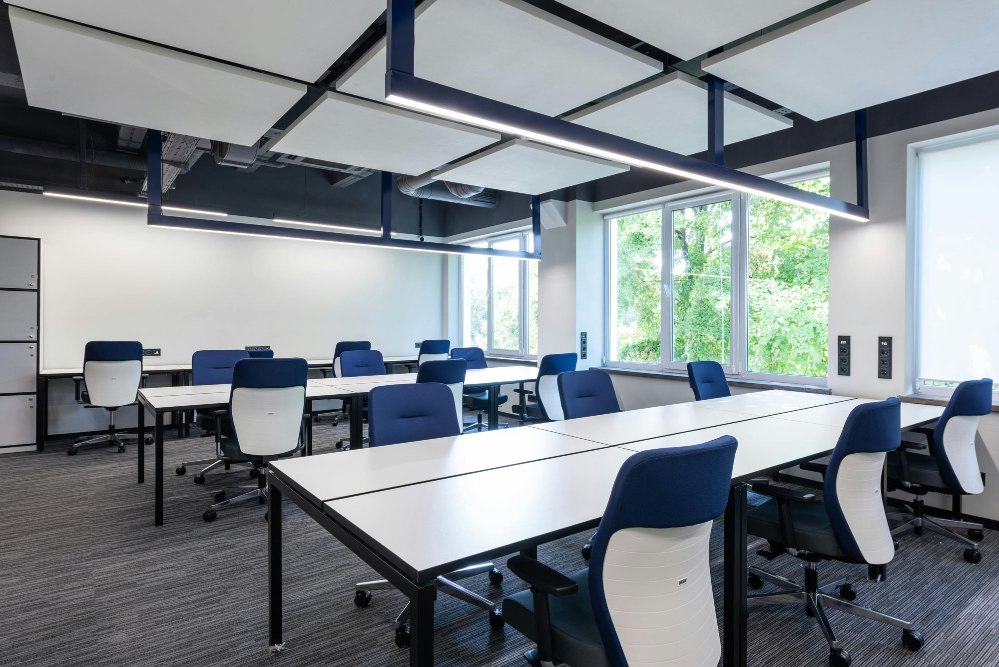 Modern office with white desks, blue chairs, large windows, and natural light streaming into the room.